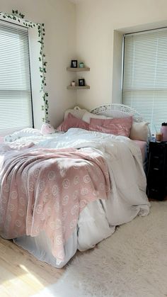 an unmade bed with pink and white comforter in a bedroom next to two windows