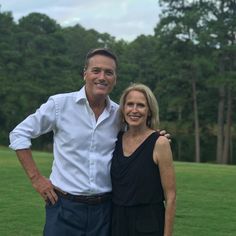 a man and woman standing next to each other in front of green grass covered field