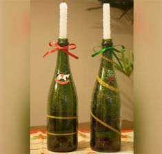 two wine bottles with candles in them on a table