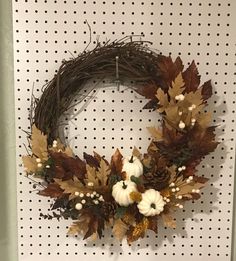 a wreath with white pumpkins and leaves hanging on a wall in front of a polka dot background