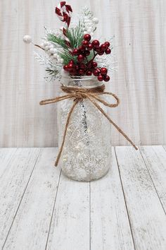 a mason jar filled with berries and greenery on a white wooden table next to a christmas ornament