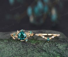 two gold rings with green and white stones sitting on top of a mossy rock