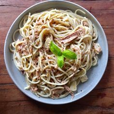 a white bowl filled with pasta and meat on top of a wooden table next to a fork