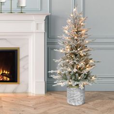 a white christmas tree in a silver pot next to a fireplace