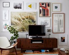 a tv sitting on top of a wooden stand in front of a wall filled with pictures