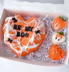 an orange heart shaped cake with white frosting in a box next to other treats