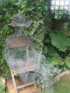 there is a sculpture made out of wire in the yard with plants growing around it