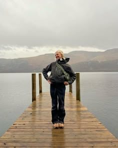 a man is standing on a dock by the water with his hands in his pockets