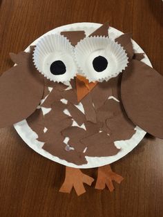 an owl made out of paper plates sitting on top of a wooden table next to a cupcake liner