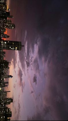 the city skyline is lit up at night with clouds in the sky and buildings on either side