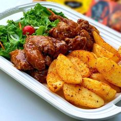 a white plate topped with meat and fries next to a green leafy salad on top of a table