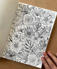 a woman's hand is holding an open notebook with flowers on the pages and black ink