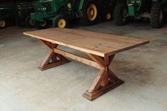 a wooden table sitting on top of a cement floor next to green tractor tractors in the background