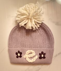 a knitted hat with flowers on the side and a pom - pom