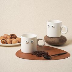 two coffee mugs sitting on top of a wooden coaster next to some cookies and nuts