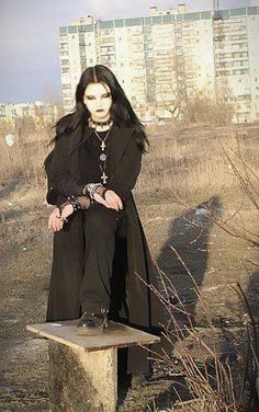 a woman sitting on top of a wooden bench in the middle of a field with tall buildings behind her