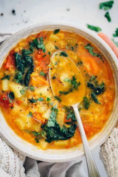 a person holding a spoon in a bowl filled with vegetable soup and spinach leaves