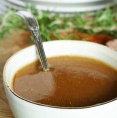 a bowl of soup with a spoon in it on a wooden table next to meat and vegetables