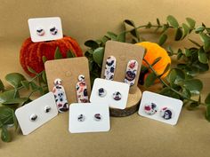 five pairs of earrings are on display in front of some leaves and pumpkins,