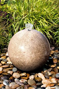 there is a large rock sitting in the middle of some rocks and gravel next to plants