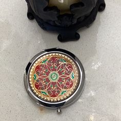 a compact mirror sitting on top of a counter next to a black object with an ornate design