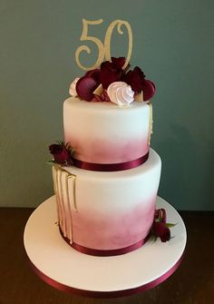 a three tiered cake with flowers on top and the number 50 written in gold