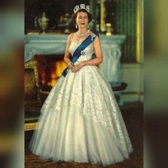 an old photo of a woman in a white dress and tiara standing next to a fireplace