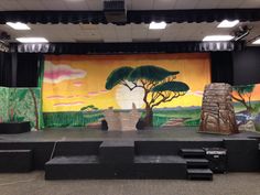 an empty stage set up for a performance with trees and mountains painted on the wall