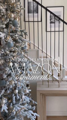 a white christmas tree with blue and silver ornaments in front of a staircase way that reads,