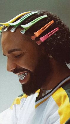 a man with long hair and colorful toothbrushes on top of his head smiling