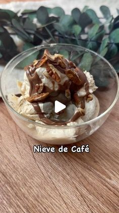 a bowl filled with ice cream and nuts on top of a wooden table next to leaves