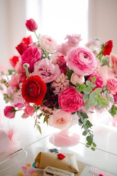 a vase filled with pink, red and white flowers next to a slice of cake