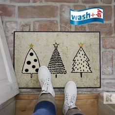 a person standing in front of a wash and dry mat with christmas trees on it