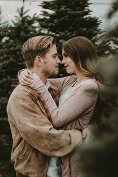 a man and woman embracing each other in front of christmas trees at the tree farm