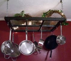 pots and pans are hanging from a rack on the wall in front of a red wall