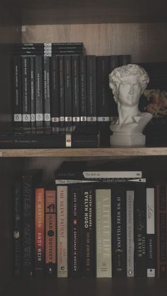 books are lined up next to a busturine on a book shelf in a library