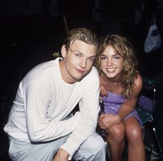 a man and woman sitting next to each other in front of a chair with their arms around one another