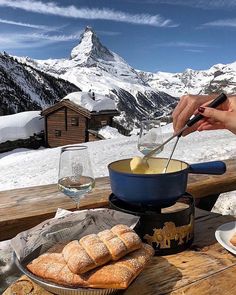 a person cooking food on top of a wooden table in the snow with mountains in the background