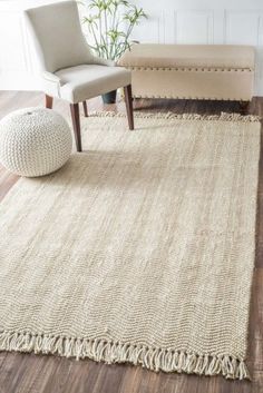 a beige rug with fringes on the floor and a chair next to it in front of a white wall