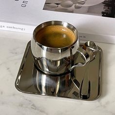 a cup of coffee sitting on top of a metal tray next to a book and spoon