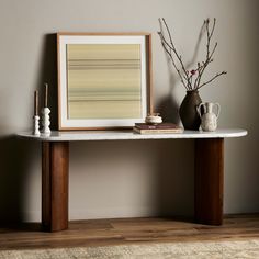 a table with vases and a painting on it next to a rug in a room