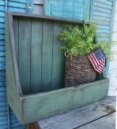 an old wooden bench has a basket with plants in it and the american flag on top