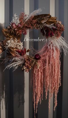 a wreath with dried flowers and feathers hanging from it's side on a wall