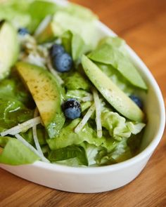 a salad with blueberries, apples and cheese in a white bowl on a wooden table