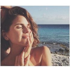 a woman is laying on the beach with her eyes closed and hands to her face