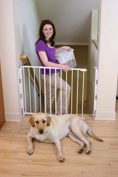 a woman standing behind a gate with a dog laying on the floor