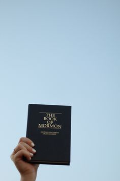 a person holding up a book in front of a blue sky with the words, the lord of the rings and mormon written on it