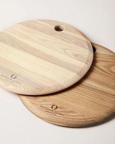 two wooden cutting boards sitting next to each other on a white surface with an oval logo