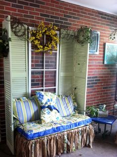 a couch sitting in front of a brick wall with shutters on each side and flowers hanging from the windows