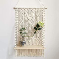 a white wall hanging with a vase and two flowers on it's shelf next to a potted plant